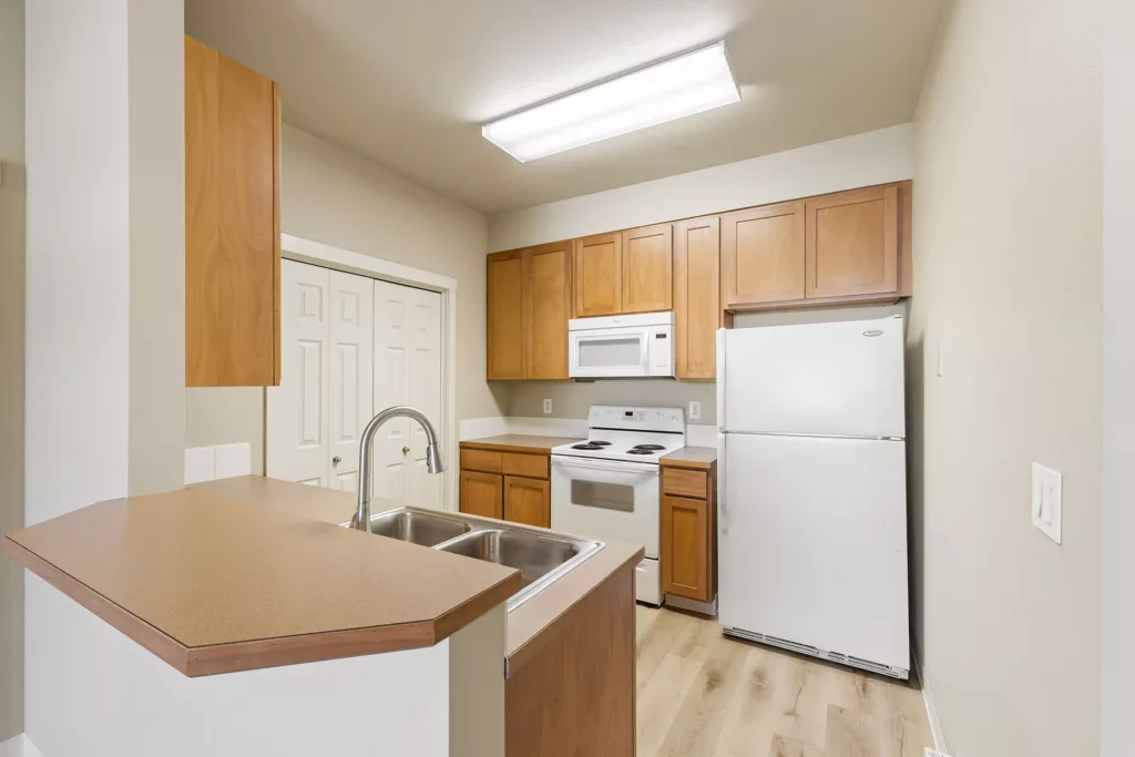 Small kitchen with wood cabinets, white fridge and stove, microwave, and double sink on a peninsula counter