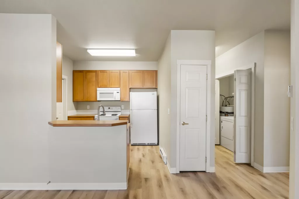 Small kitchen with wood cabinets, white appliances, breakfast bar, and a laundry closet with washer and dryer.