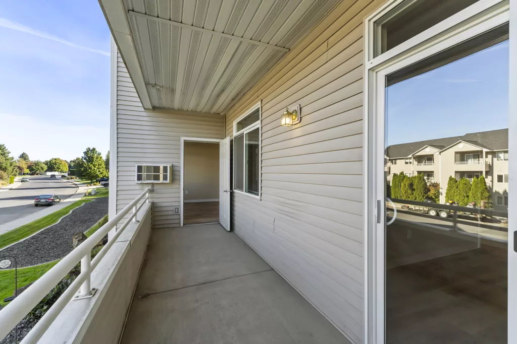 Covered apartment balcony with railing, open door and window, and view of street and nearby buildings