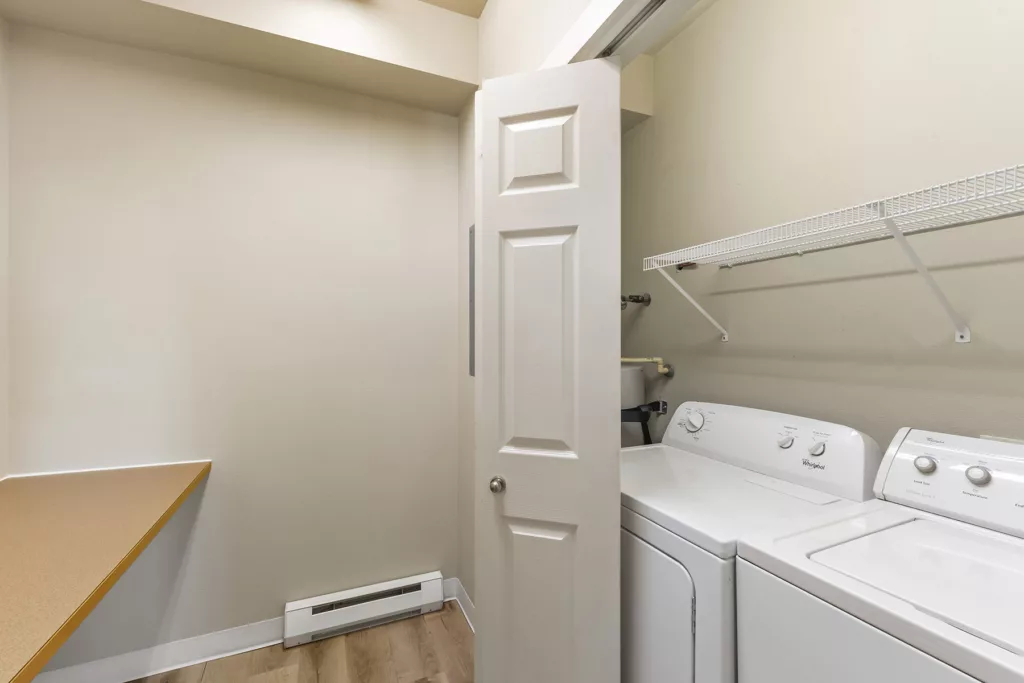 Laundry closet with washer and dryer, wire shelf above, and a countertop folding area to the left