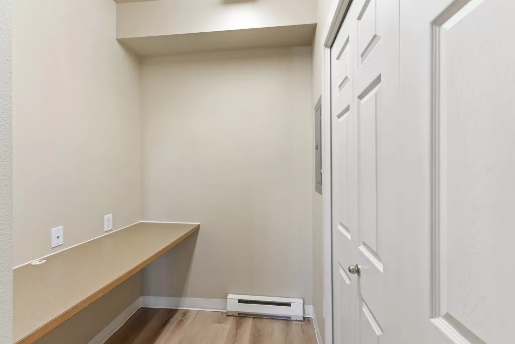Small empty alcove with a built-in counter desk, beige walls, wood floor, and white closet doors on the right.