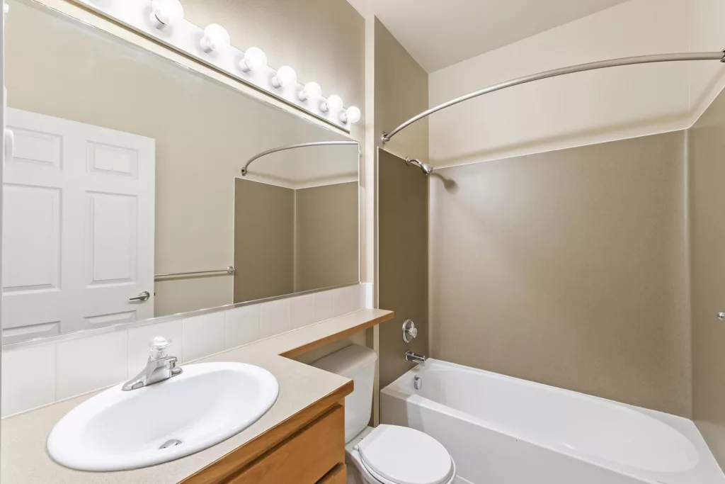 Bathroom with sink and large mirror, toilet, and bathtub shower with curved curtain rod and beige walls.