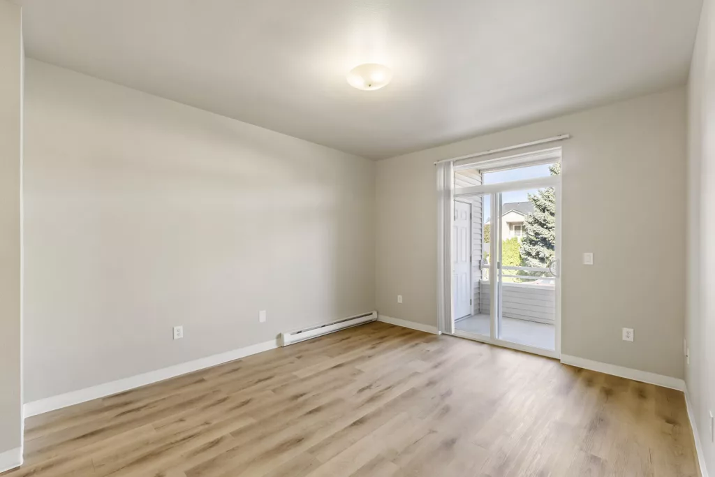 Empty room with light wood floors, beige walls, ceiling light, and sliding glass door to a small balcony.