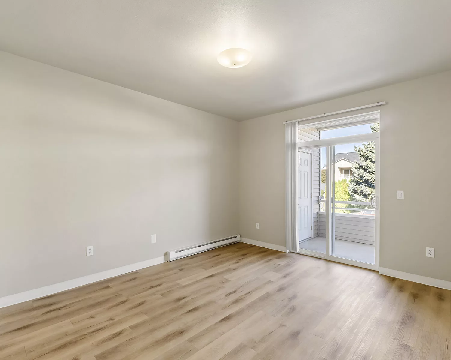 Empty room with wood-look flooring and sliding glass door opening to a small balcony with daylight view