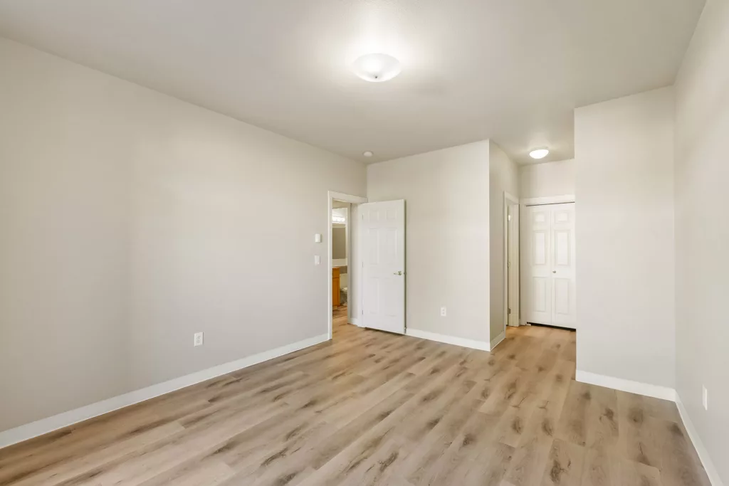 Empty room with light wood floors, beige walls, ceiling lights, and open door to a hallway and closet.