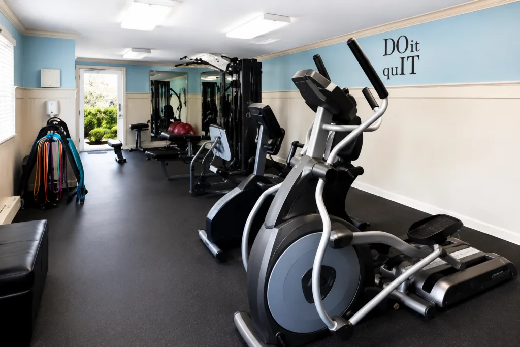 Small gym room with an elliptical machine, weight station, bench, resistance bands, and a wall quote reading Do it quIT.